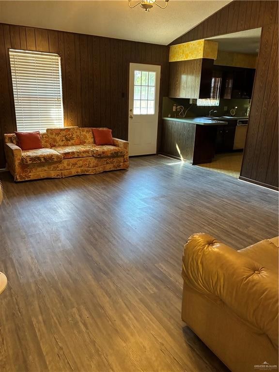 Living room featuring wooden walls, vaulted ceiling, wood finished floors, and a chandelier
