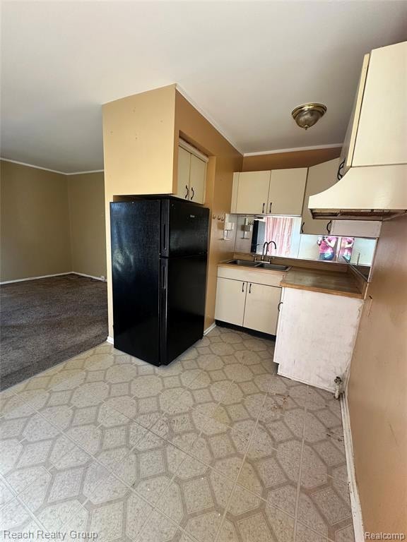Kitchen with freestanding refrigerator, crown molding, light countertops, extractor fan, and light carpet