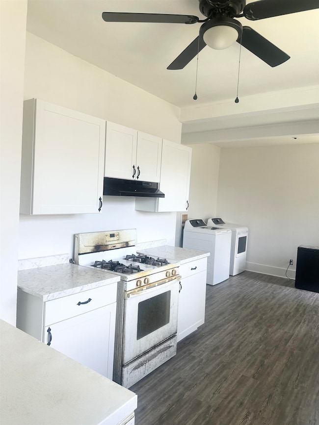 Kitchen with range with gas stovetop, washer and clothes dryer, under cabinet range hood, light countertops, and ceiling fan