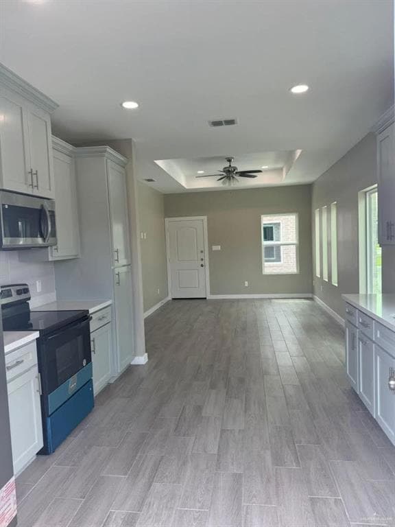 Kitchen featuring a raised ceiling, electric range oven, stainless steel microwave, light wood finished floors, and open floor plan