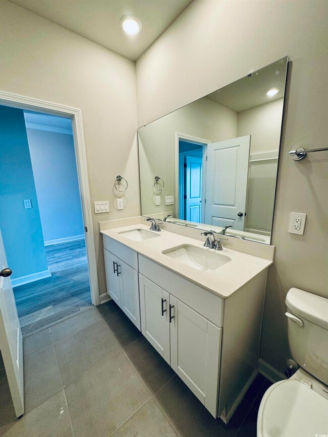 Bathroom with toilet, a sink, tile patterned floors, and double vanity
