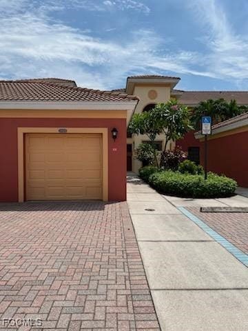 Mediterranean / spanish home featuring stucco siding, a tiled roof, a garage, and decorative driveway
