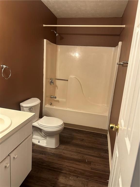 Bathroom with dark wood-style floors,  shower combination, vanity, and a textured ceiling