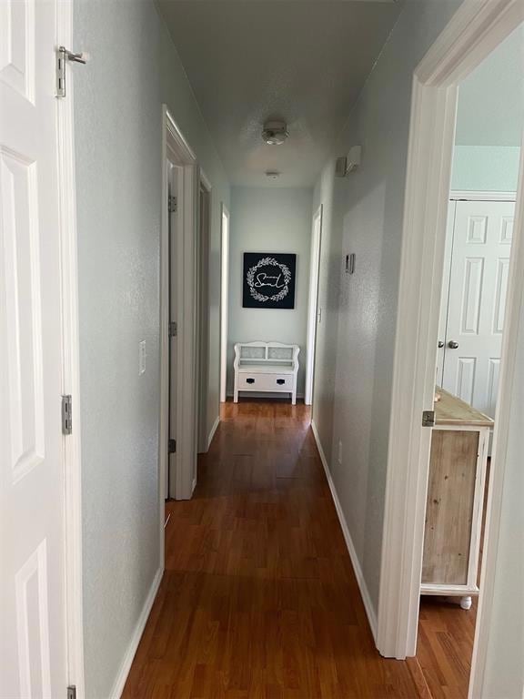 Hall with dark wood-type flooring and baseboards