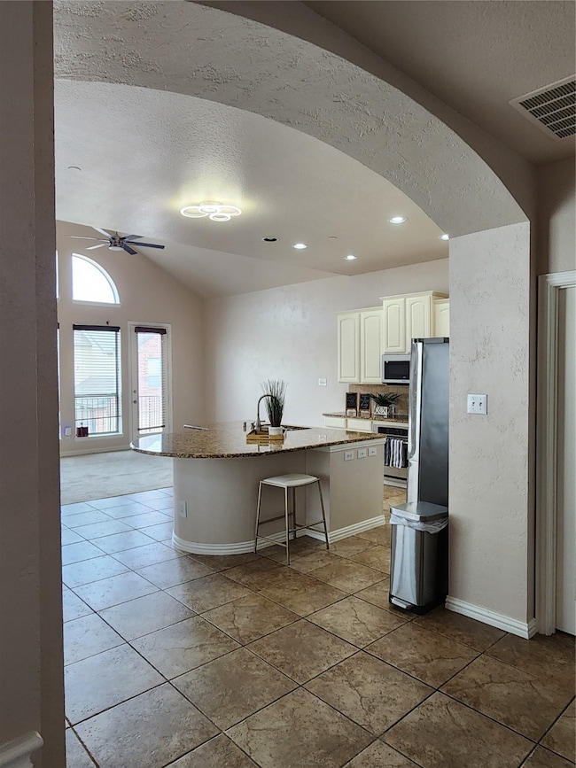 Kitchen featuring a kitchen breakfast bar, vaulted ceiling, light stone counters, an island with sink, and a textured ceiling