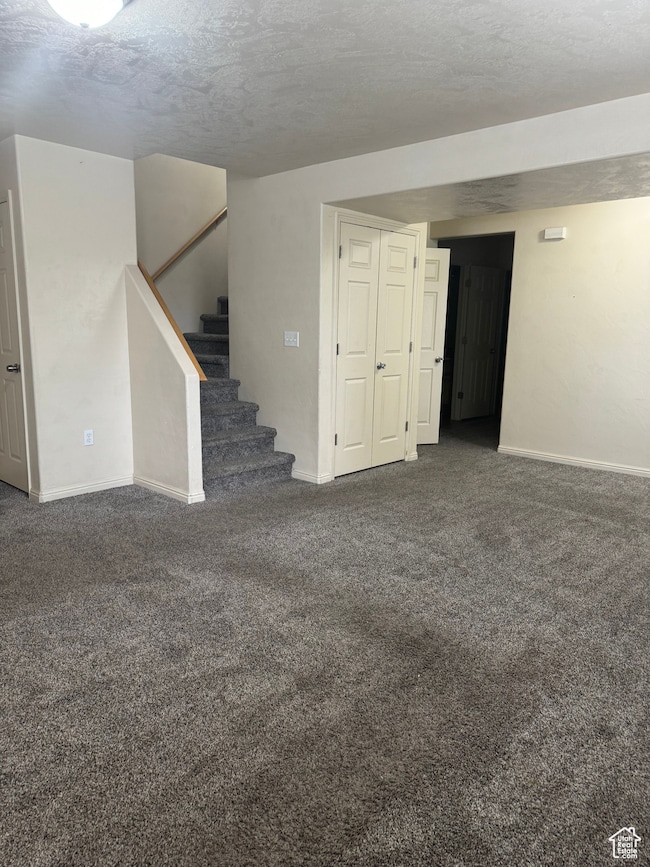 Basement with a textured ceiling and dark colored carpet