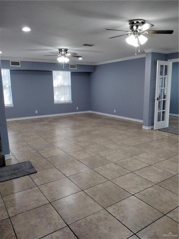 Spare room with crown molding, baseboards, a ceiling fan, and visible vents