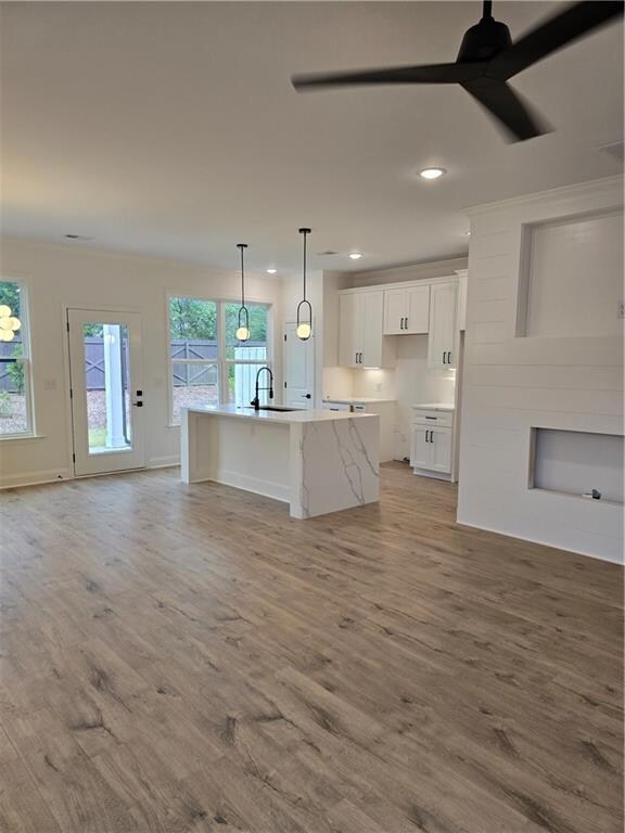Kitchen featuring a center island with sink, white cabinets, open floor plan, hanging light fixtures, and light wood-type flooring
