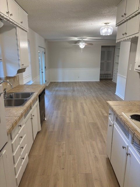 Kitchen with light wood-style floors, tile counters, white cabinetry, a textured ceiling, and wainscoting
