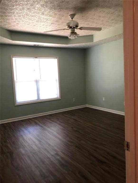 Empty room with dark wood-style flooring, ceiling fan, and a textured ceiling