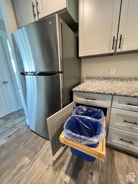 Kitchen with freestanding refrigerator, wood finished floors, light stone countertops, and white cabinetry