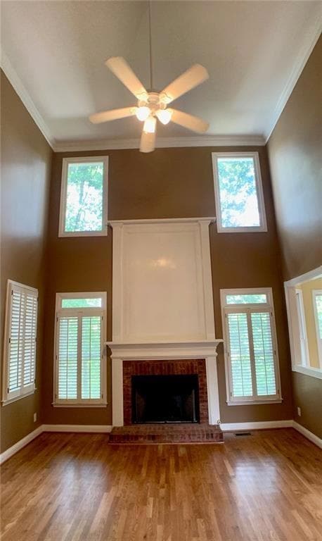 Unfurnished living room featuring a towering ceiling, a brick fireplace, crown molding, light wood finished floors, and a ceiling fan