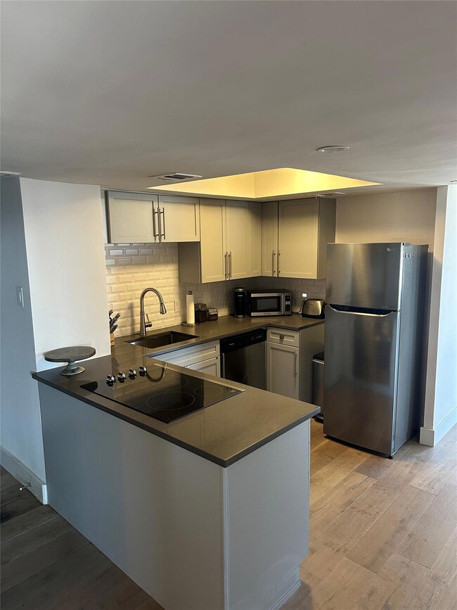 Kitchen with dark countertops, appliances with stainless steel finishes, light wood finished floors, and a peninsula