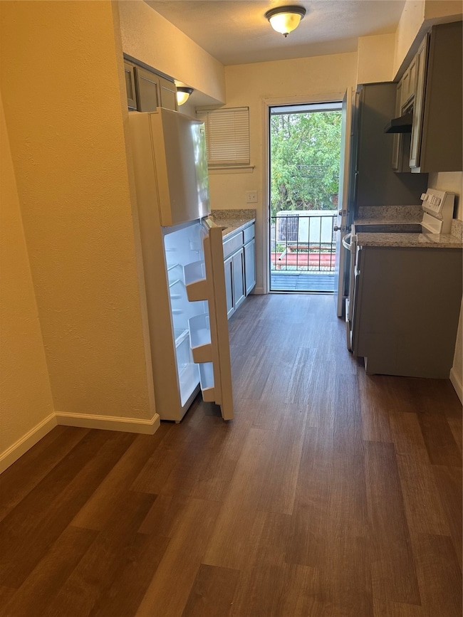 Kitchen featuring stove, light stone countertops, dark wood-style flooring, a textured wall, and exhaust hood