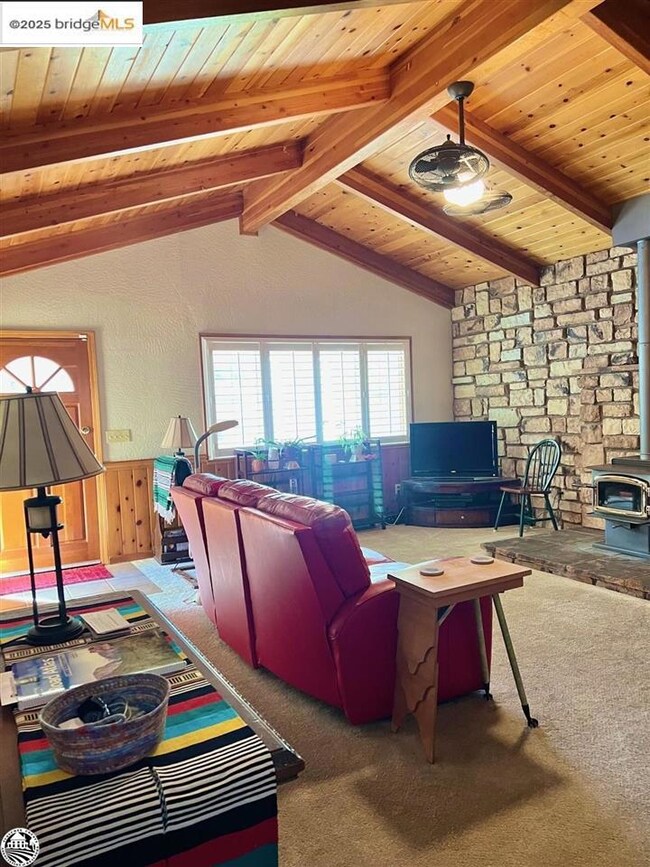Carpeted living room with wooden ceiling, lofted ceiling with beams, and a wood stove