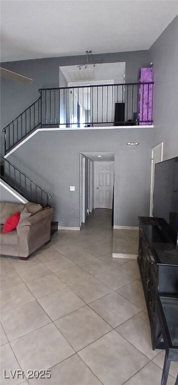 Tiled living room with stairs, a towering ceiling,