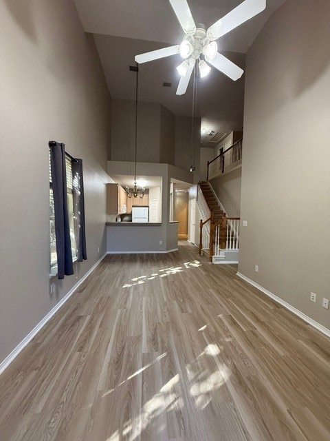 Unfurnished living room with a chandelier, stairway, wood finished floors, ceiling fan, and high vaulted ceiling
