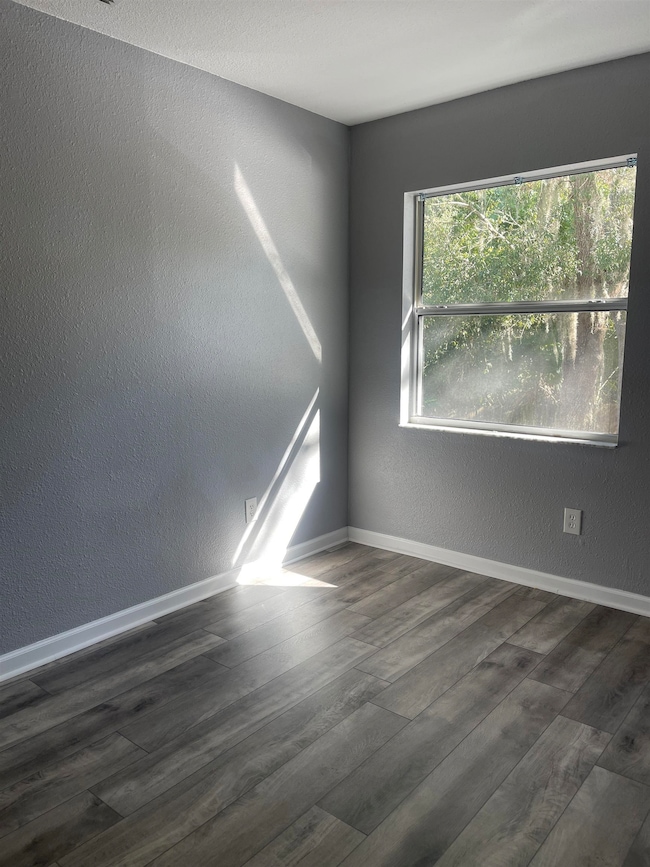 Empty room featuring a textured wall and dark wood finished floors
