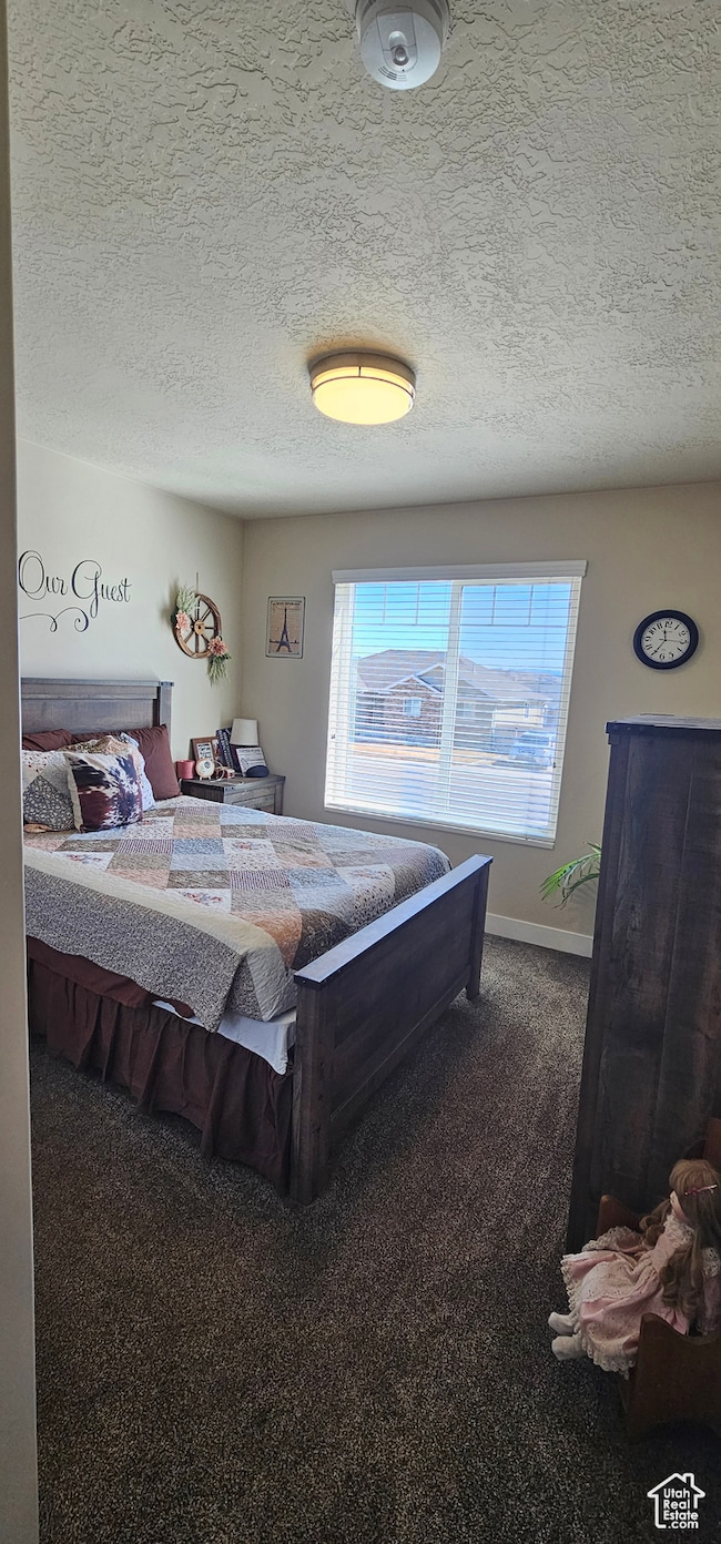 Bedroom with dark colored carpet, a textured ceiling, and multiple windows