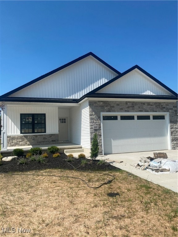 View of front facade with stone siding, an attached garage, and a porch