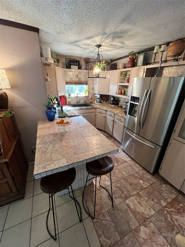 Kitchen with open shelves, pendant lighting, fridge, a breakfast bar, and a textured ceiling