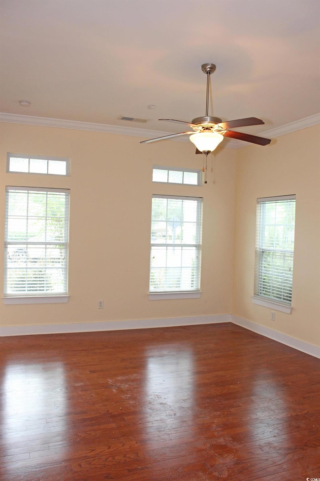Empty room with ornamental molding, healthy amount of natural light, and dark wood-style floors