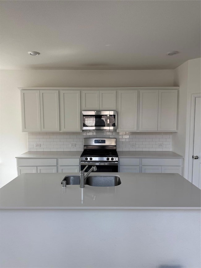 Kitchen with stove, white cabinets, light countert