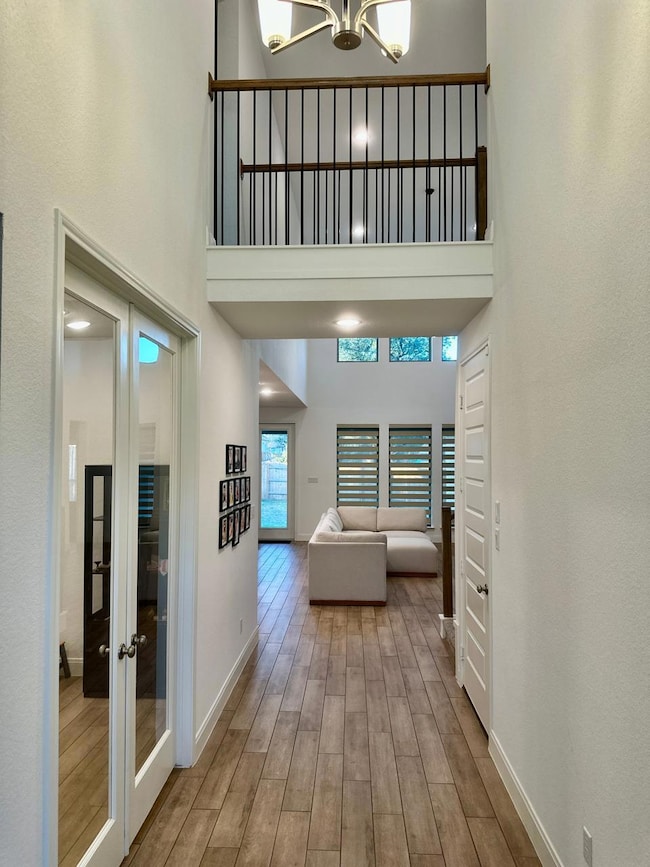 Hallway with a towering ceiling, light wood finished floors, and a chandelier