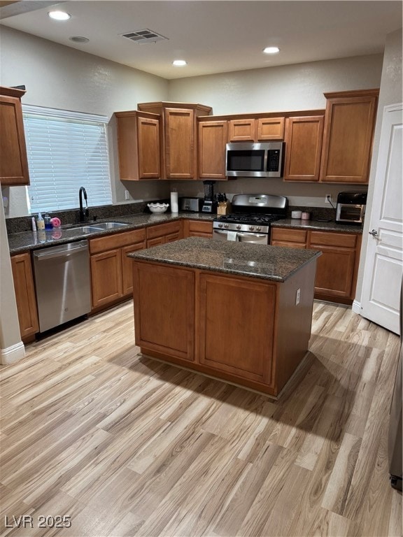 Kitchen featuring range, light wood-style floors, dark stone counters, brown cabinetry, and dishwasher
