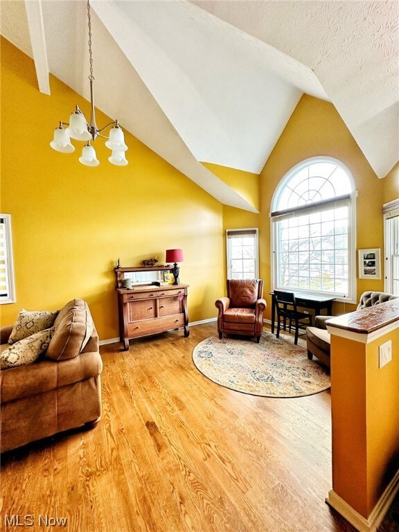 Living room featuring a notable chandelier, a textured ceiling, light hardwood / wood-style floors, and high vaulted ceiling