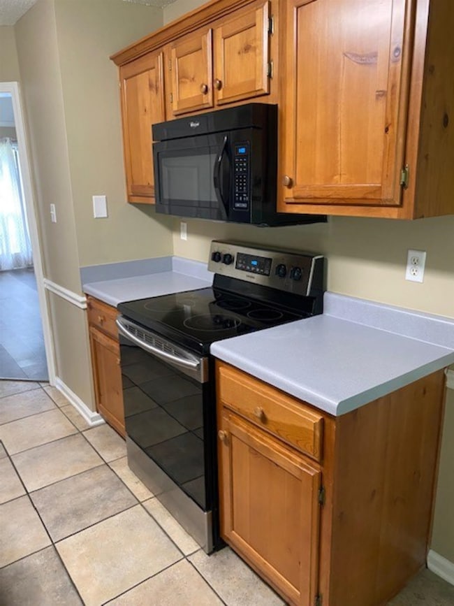 Kitchen featuring  range with electric stovetop, black microwave, light countertops, brown cabinetry, and light tile patterned floors