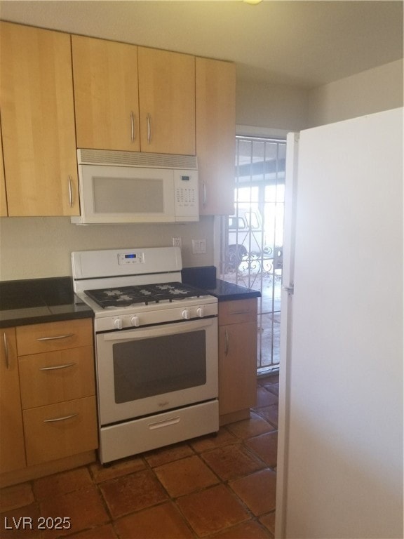 Kitchen with dark countertops, white appliances, dark tile patterned flooring, and light brown cabinets