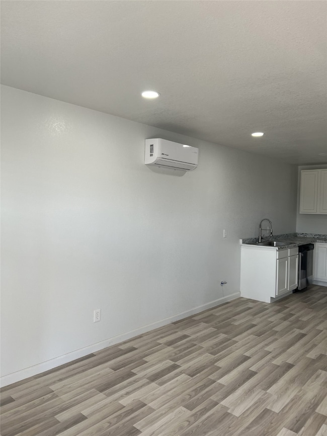 Kitchen with white cabinetry, light wood-style flooring, recessed lighting, stainless steel dishwasher, and a wall mounted air conditioner