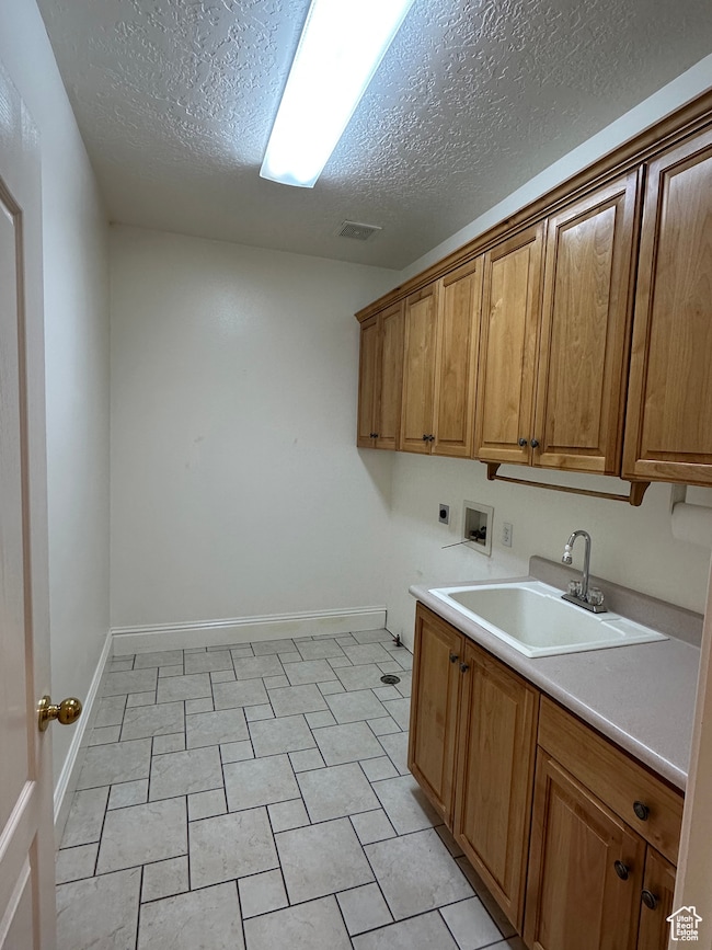 Laundry room featuring hookup for a washing machine, cabinet space, a textured ceiling, hookup for an electric dryer, and light tile patterned flooring