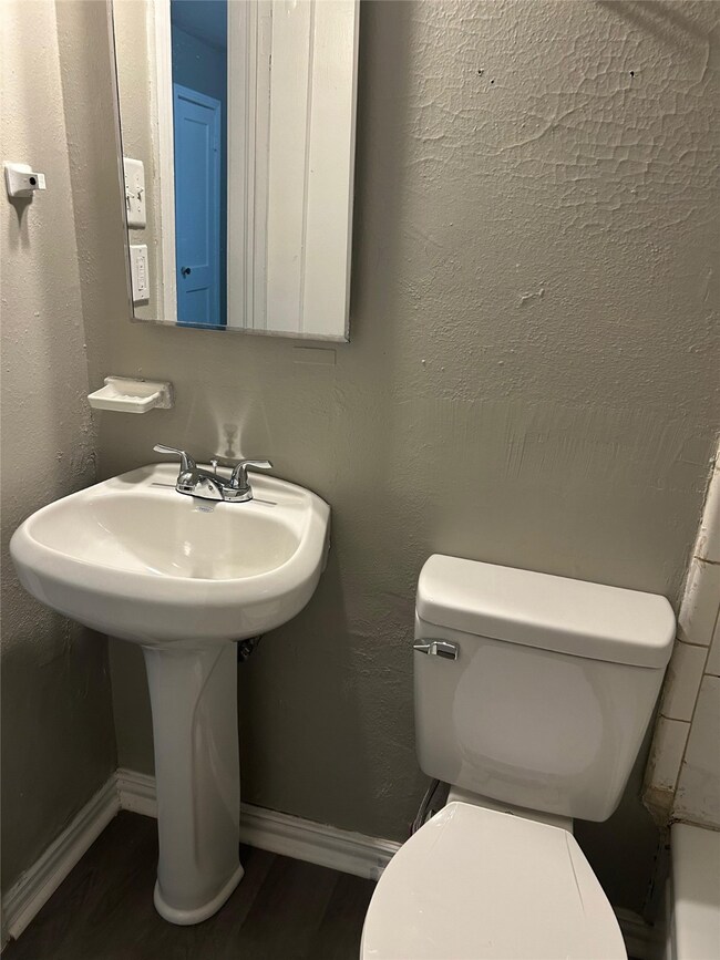 Half bathroom with a textured wall and dark wood-style floors