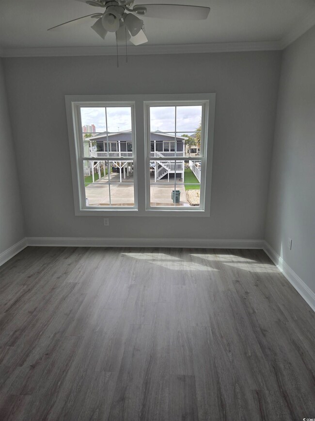 Spare room with a ceiling fan, crown molding, dark wood-style floors, and baseboards