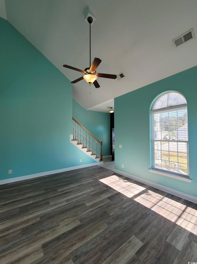 Unfurnished living room with vaulted ceiling, wood finished floors, ceiling fan, and stairs