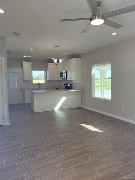 Kitchen featuring white cabinets, a wealth of natural light, ceiling fan with notable chandelier, and backsplash