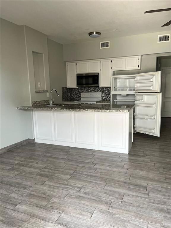 Kitchen with white cabinets, appliances with stainless steel finishes, dark wood-type flooring, and dark stone countertops