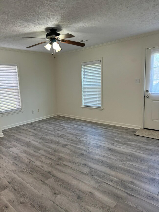 Spare room with a textured ceiling, wood finished floors, ceiling fan, crown molding, and baseboards