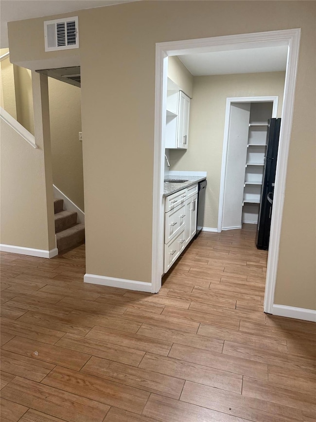 Kitchen with white cabinets, light wood-type flooring, light stone counters, stainless steel dishwasher, and freestanding refrigerator