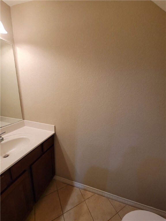 Half bathroom featuring vanity, light tile patterned floors, and a textured wall