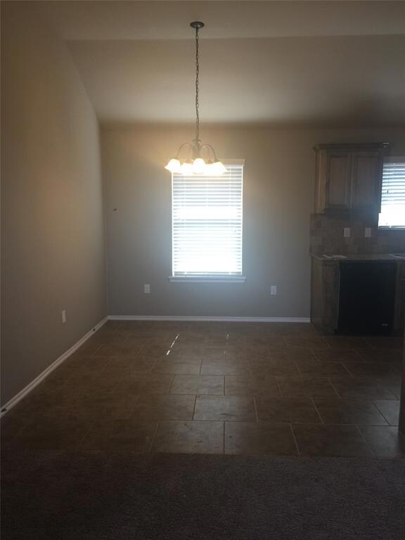 Unfurnished room featuring a chandelier and baseboards