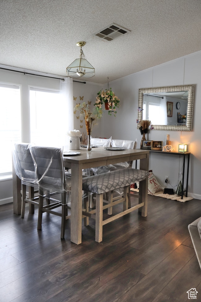 Dining space with a textured ceiling, dark wood-style floors, and ornamental molding