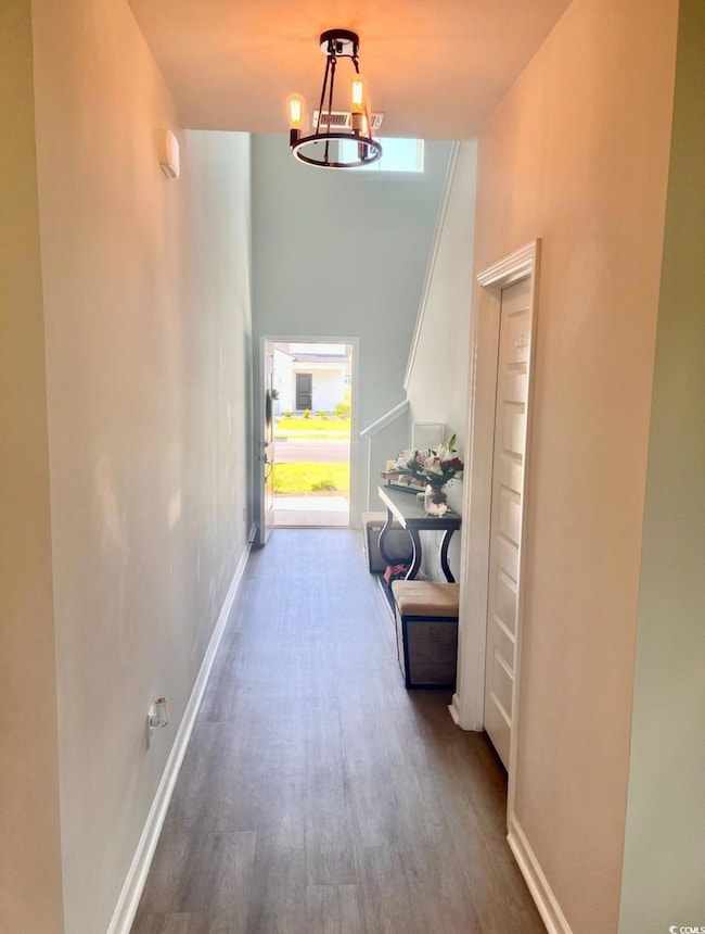 Hall with wood finished floors, plenty of natural light, a high ceiling, and baseboards