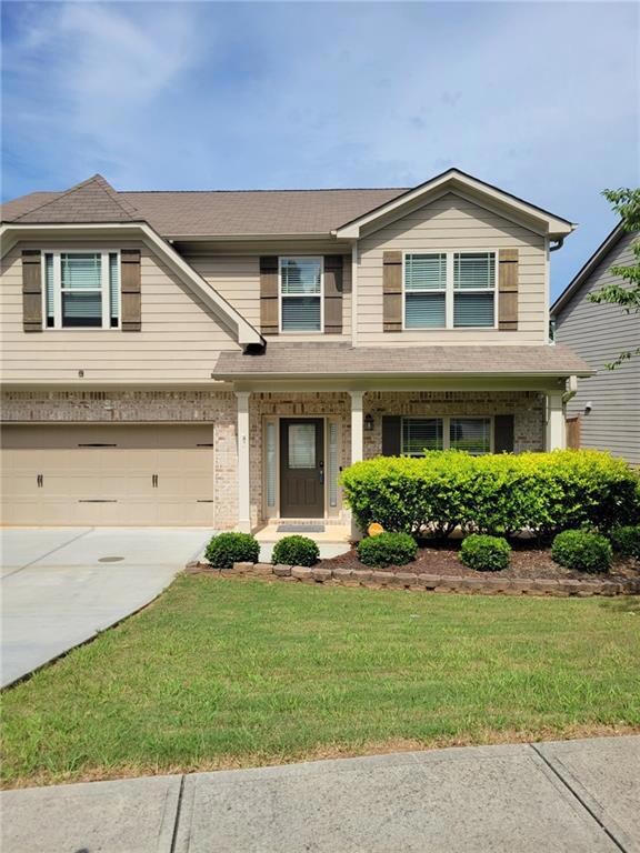 View of front of property with concrete driveway, a front lawn, an attached garage, covered porch, and brick siding
