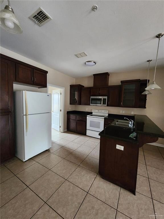 Kitchen featuring decorative light fixtures, sink, white appliances, and dark brown cabinetry