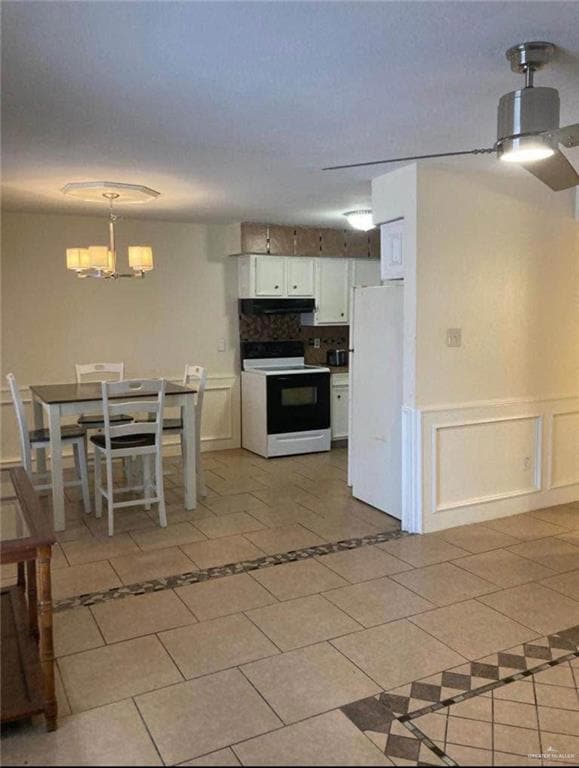 Kitchen with freestanding refrigerator, white cabinets, under cabinet range hood, a notable chandelier, and electric range oven