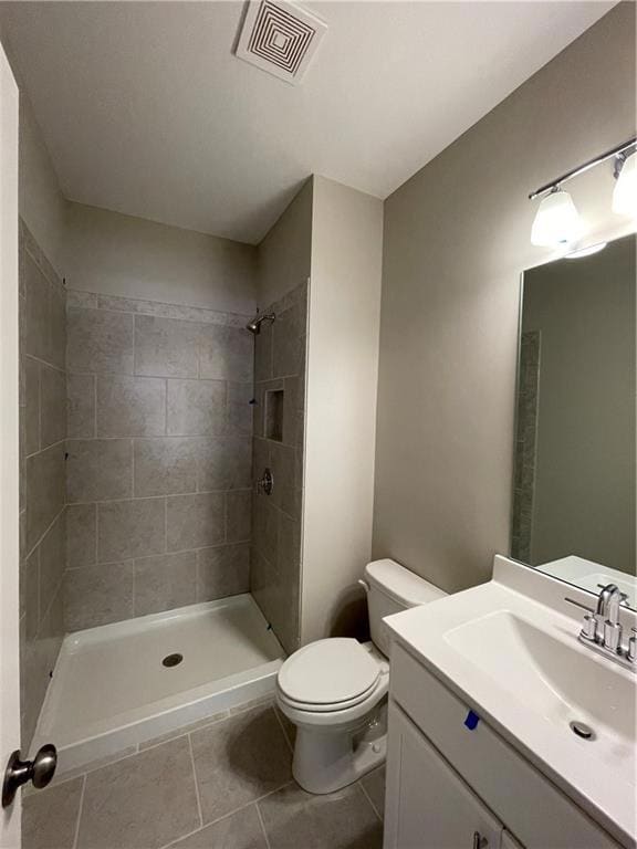 Full bathroom featuring a tile shower, toilet, vanity, and tile patterned floors