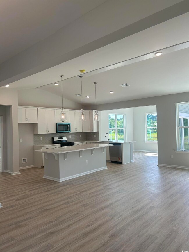Kitchen featuring stainless steel appliances, a center island, white cabinetry, light wood-style flooring, and lofted ceiling